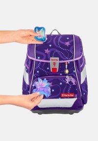 Sac à dos violet avec un motif d'étoile en tourbillon, doté d'accessoires amovibles : une fée bleue et une licorne violette. Éléments réfléchissants et base robuste.