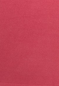 Stickad tyg i en enhetlig rosa färg, med en slät yta och subtila ribbor. Inga påtagliga mönster eller detaljer finns.