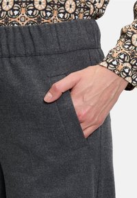 Grå tygbyxor med mjuk textur och elastisk midja, med en sidoficka där en hand vilar.