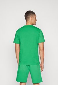 Groene katoenen t-shirt met korte mouwen, ronde halslijn en een gladde textuur, gecombineerd met bijpassende groene shorts. Eenvoudig, effen ontwerp.