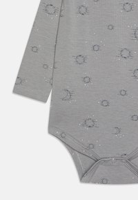 Szürke, hosszú ujjú body, puha textúrával, szétszórt sötétkék kör- és csillagmintákkal, és patentos záródással az alján.