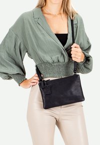 Black leather crossbody bag with a textured finish, rectangular shape, detachable strap, and a small tag attached to the zipper.