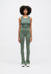 Πράσινη κοντή τοπ με υφή, συνδυασμένη με εφαρμοστά πράσινα κολάν. Τα κολάν έχουν φαρδύ στρίφωμα και είναι φτιαγμένα από λείο ύφασμα.