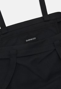 Sac cabas en tissu noir avec des anses doubles et une petite étiquette noire portant la mention "even&ODD" cousue près du bord supérieur.