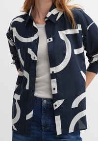 Chemise boutonnée marine avec des motifs abstraits blancs, manches longues retroussées et col, fabriquée dans un tissu léger.