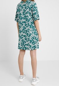 Vestido de estampado floral en tejido verde azulado, con mangas cortas y corte holgado. Patrón notable de flores blancas por toda la prenda, combinado con zapatillas con acentos plateados.