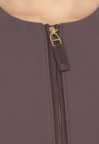 Indumento con zip in ricco tessuto mauve; presenta una zip dorata con un tirante in pelle; superficie liscia e scollatura rotonda.