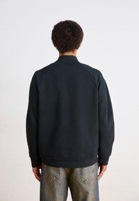 Sudadera negra con cuello y puños de canalé, con una textura suave y mangas raglán, combinada con jeans de mezclilla de lavado claro.