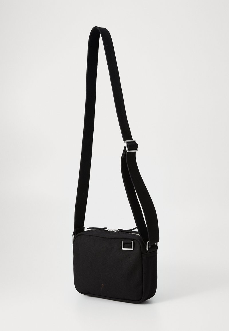 Bolso cruzado negro hecho de tela, con forma rectangular, cierre de cremallera y una correa ajustable con un broche metálico.