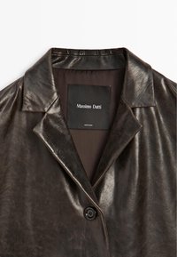Bruine leren jas met een gekartelde kraag, enkele zwarte knoopsluiting en een gladde textuur. Het label toont 'Massimo Dutti'.
