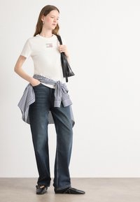 Hvid kortærmet T-shirt med et trykt mærke, afslappede mørkeblå jeans, stribet skjorte bundet om taljen og sorte flade sko.