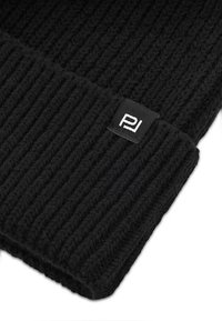 Czarna dzianinowa czapka beanie o prążkowanej fakturze. Posiada małą metkę z białym logo. Materiał wydaje się miękki i ciepły.