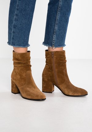 Brune ruskindsankelstøvler med sidelås og chunky hæl, båret med korte blå denimjeans med frynset kant.