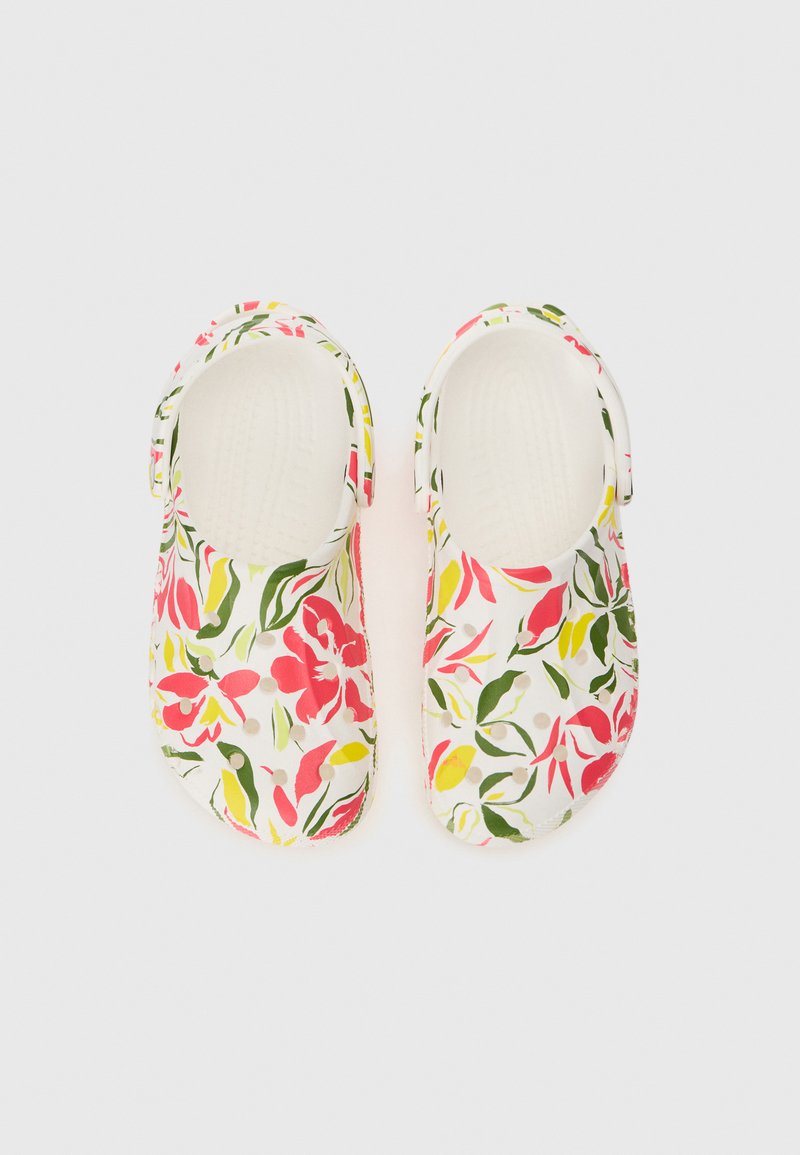 Een paar witte instapklompen met een roze, gele en groene bloemenpatroon en verstelbare hielbandjes op een witte achtergrond.