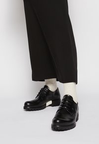 Chaussures en cuir noir avec une finition brillante, à bout rond et semelle en caoutchouc épaisse. Détails en lacets noirs et accent blanc sur le talon.