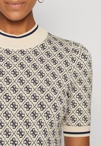 Pull à manches courtes en crème avec motif géométrique bleu marine et col côtelé. Présente des rayures contrastées sur les manches. Tissu texturé.