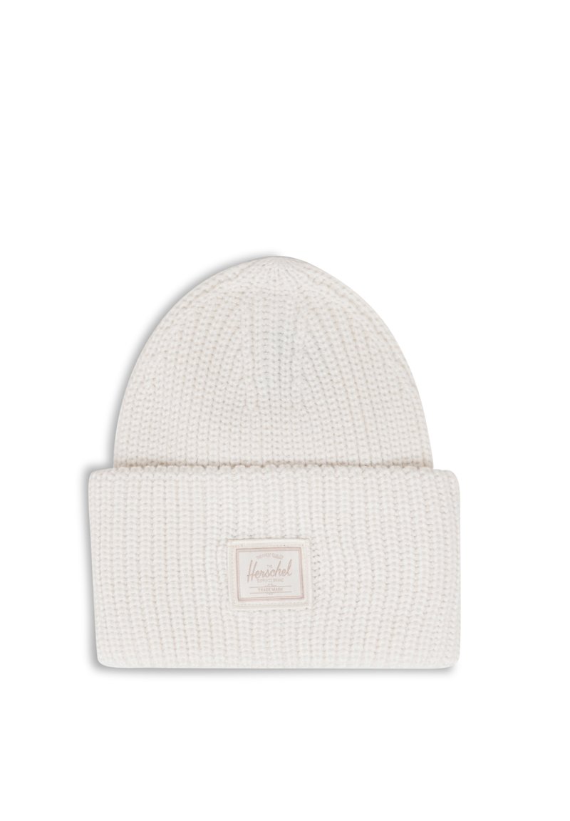 Bonnet en tricot blanc avec un revers plié, arborant une étiquette de marque rectangulaire dans une teinte beige douce. Motif texturé sur l'ensemble du tissu.