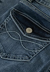 Jean en denim bleu foncé avec une poche arrière détaillée, présentant des coutures courbées et un accent en bouton métallique. La texture semble lisse et durable.