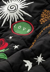 Fekete steppelt szövet színes hímzett foltokkal: egy spirál nap, egy piros rózsa, zöld "SZERETET" felirat, valamint párducmintás díszítések.