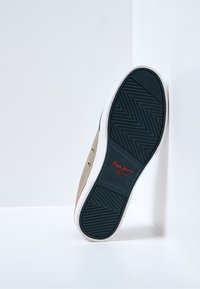 Baskets en toile beige avec une semelle blanche, motif zigzag bleu marine en bas, et logo rouge "Pepe Jeans London" sur le côté.
