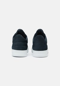 Paire de baskets basses noires avec semelles blanches vues de dos sur un fond blanc uni.