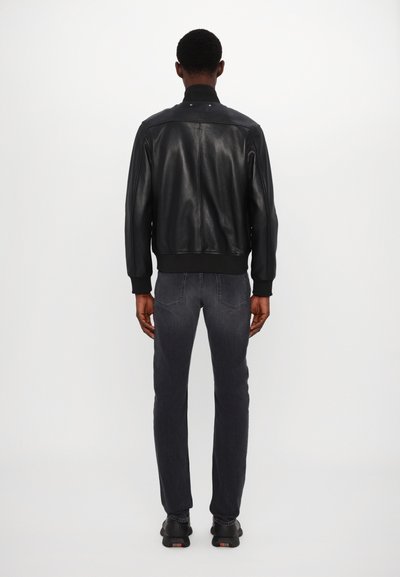 Μαύρη δερμάτινη bomber τζάκετ με ριμπ μανσέτες και στρίφωμα, συνδυασμένη με σκούρα γκρι τζιν και μαύρα παπούτσια, προσανατολισμένη από πίσω.