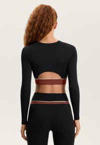 Fekete, hosszú ujjú sportfelső hátsó kivágással, fekete magas derekú leggingsszel, piros és fehér díszítő szalagokkal.