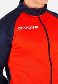 Rdeča in mornarsko modra športna jakna z zadrgo spredaj, visokim ovratnikom in logotipom "GIVOVA". Gladka tekstura in kontrastni barvni paneli.