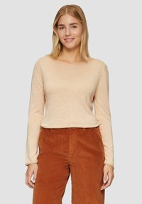Helles beige Langarmoberteil mit weitem Ausschnitt und weicher Textur. Kombiniert mit rostfarbenen Cordhosen mit vertikalen Rillen.