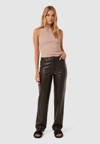 Débardeur à côtes beige clair associé à un pantalon en simili cuir noir taille haute et des sandales noires à enfiler. Coupe droite avec poches avant.