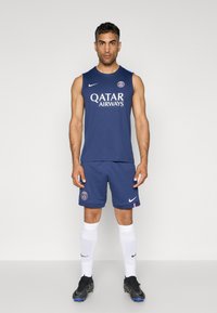 Kit de sport marine comprenant un maillot sans manches avec le logo "Qatar Airways" et un short assorti. Inclus des chaussettes blanches montantes et des chaussures de sport noires.