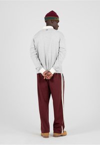 Sivá dlhá rukávová košeľa s bielymi manžetami, gaštanové nohavice so bočnými pruhmi a gaštanová čiapka s zelenými akcentmi. Voľný strih.