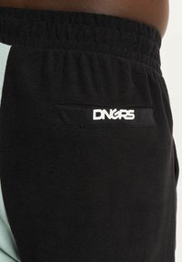 Čierne joggers s bledomodrým panelom, elastickým pásom a zadnou vreckom s bielym logom. Textúrovaná tkanina, voľný strih.