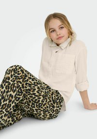 Světle béžová košile na knoflíky s kapsou na prsou, spárovaná s širokými kalhotami s leopardím potiskem v černé a béžové barvě. Hladká, prodyšná tkanina.