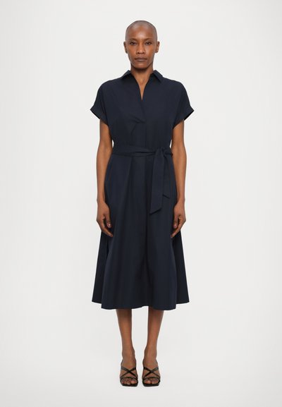 Robe bleu marine à manches courtes, avec ceinture à la taille et jupette évasée. Tissu lisse avec une silhouette épurée, sans motifs visibles.