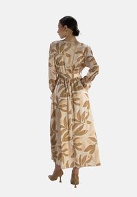 Robe longue avec ceinture en tissu léger, ornée d'un imprimé de feuilles aux teintes chaudes. Le design présente des manches longues et une silhouette fluide.