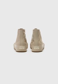 Baskets montantes en toile beige avec semelles en caoutchouc, dotées d'un patch logo circulaire sur le côté et de la marque "Converse All Star" sur le talon.