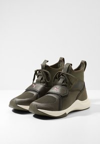 Green athletic shoes with mesh and smooth fabric, featuring a pink logo accent and a textured sole. High-top design with lace closure.