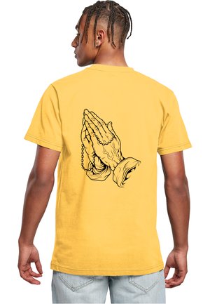 Geel katoenen t-shirt met een zwarte graphic van twee biddende handen die een rozenkrans vasthouden op de achterkant. Korte mouwen, casual pasvorm.
