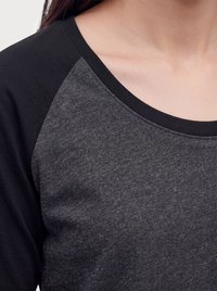 Primer plano de una persona que lleva una camiseta de manga larga en dos tonos, gris y negro, con un cuello redondo ancho que muestra parte del cuello y del hombro.