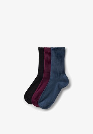 Drie paar geribbelde enkelsokken in zwart, bordeauxrood en marineblauw, netjes opgestapeld op een witte achtergrond.