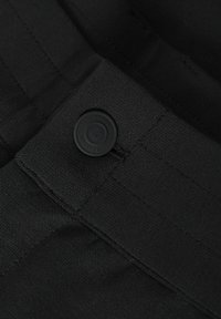 Crni materijal s glatkom teksturom, s istaknutim crnim gumbom na pojasu i šivenim detaljima za pojačanje.