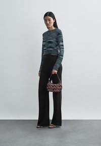 Μακρύ μαύρο παντελόνι με σχέδιο, εφαρμοστό μπλε τοπ με ρίγες και μια μικρή πολύχρωμη τσάντα. Φοράει σανδάλια με υφή στη σόλα.