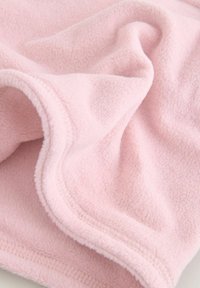 Svetloružový fleece prikrývka s mäkkým, textúrovaným povrchom a prešitým okrajom, zložená tak, aby odhalila záhyby a vrstvy.