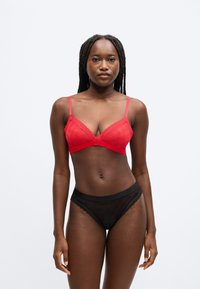 Bralette de renda vermelha com alças ajustáveis, apresentando um padrão floral, combinado com cuecas de renda preta transparente com acabamento festonado.