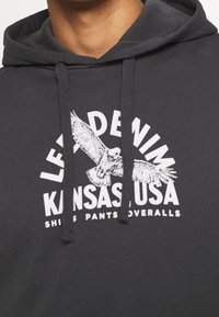 Felpa con cappuccio grigia scura con stampa grafica di un uccello in volo e testo che recita "LEVI'S DE NIM KANSAS USA." Presenta cordini.