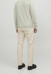 Béžové bavlněné kalhoty a světle šedý svetr s kulatým výstřihem, dlouhými rukávy a slim fit. Celkový vzhled doplňují tmavé boty.