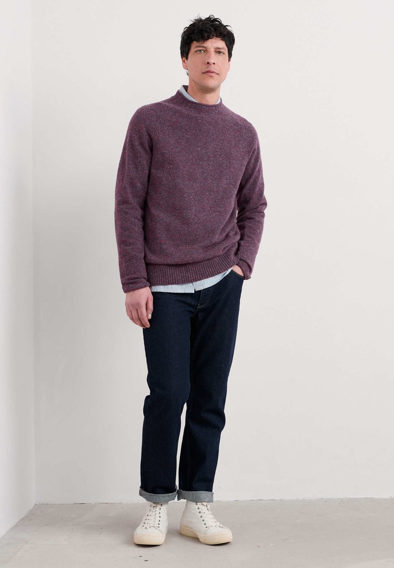 Bordo adīts džemperis ar augstu kaklu, valkāts virs gaiši zilas krekla. Apvienots ar tumšiem džinsu biksēm un krēmkrāsas kedām.