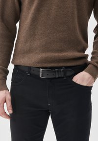 Fekete bőr öv téglalap alakú ezüst csattal, barna textúrált pulóverrel és fekete nadrággal viselve, bemutatva egy laza ruházati részletet.