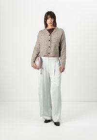 Lysegrå sateng vide bukser parret med en cropped beige strikket cardigan med mørke knapper, og en lille lyserød håndtaske.